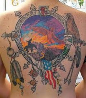 Elaborate Native American Tattoo of a scene of an American Indian mounted on a horse atop a cliff with a bird spirit in the sky. The scene is viewed the a kind of lens which is decorated with a buffalo skull, a bird, feathers, arrowheads, and other Native American cultural symbols.