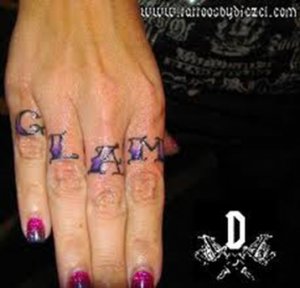 A tattoo written in olde english lettering on the fingers of the word Glam